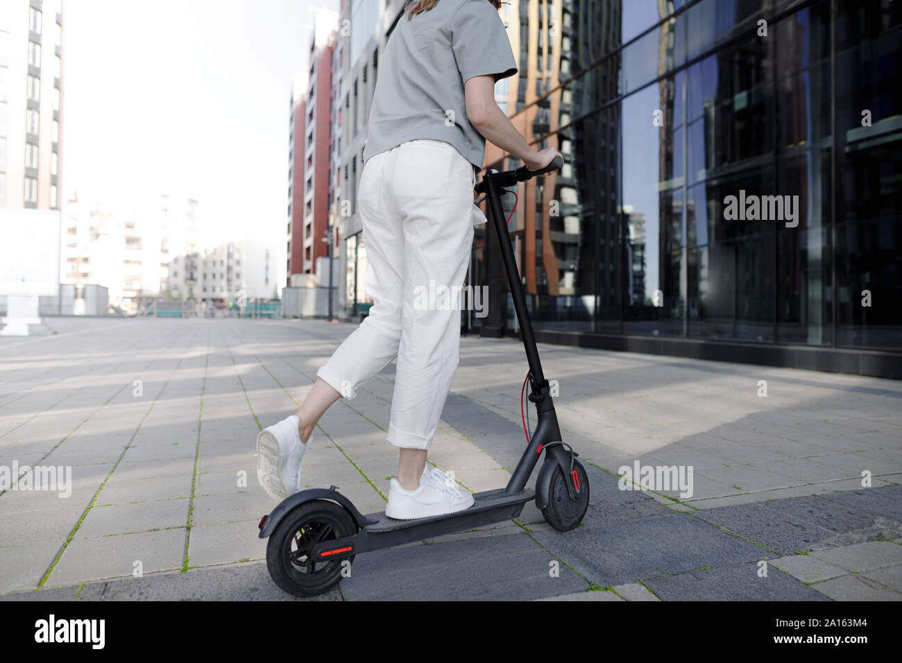 Giovane donna su e-scooter, edifici moderni in background Foto Stock