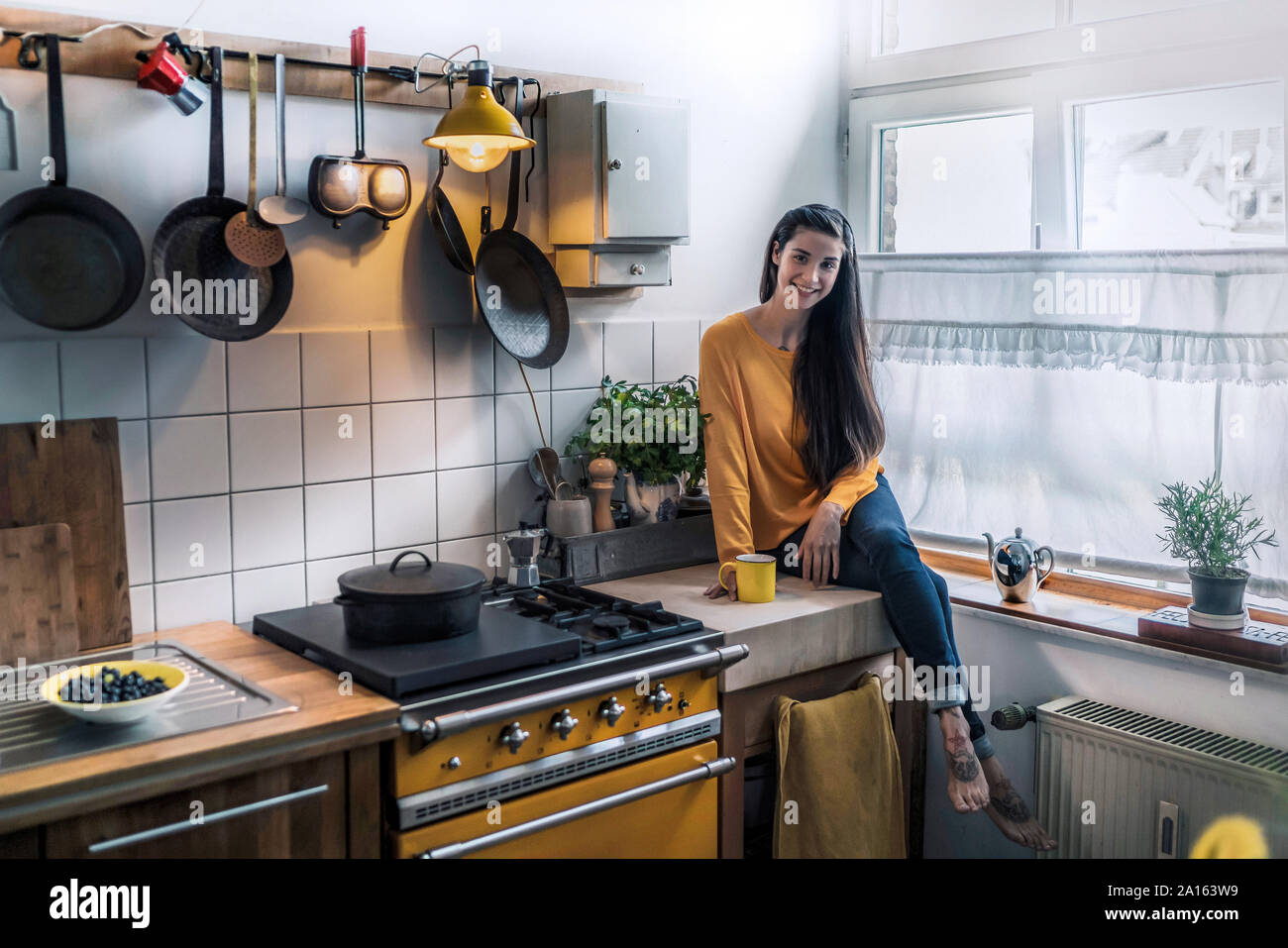 Ritratto di giovane sorridente donna seduta sul banco di cucina a casa Foto Stock