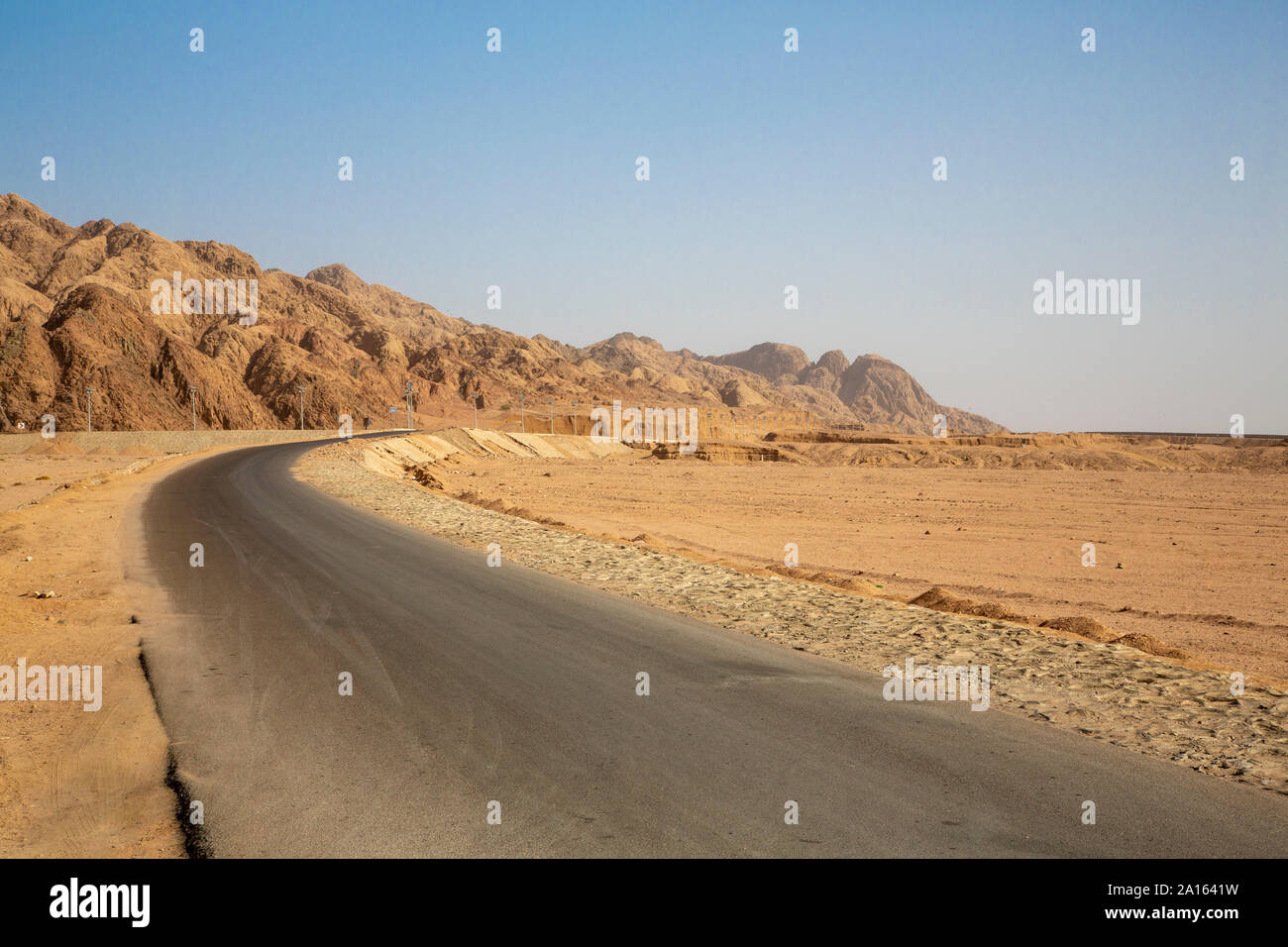 Strada vuota dalla formazione di roccia nel deserto contro il cielo blu chiaro Foto Stock