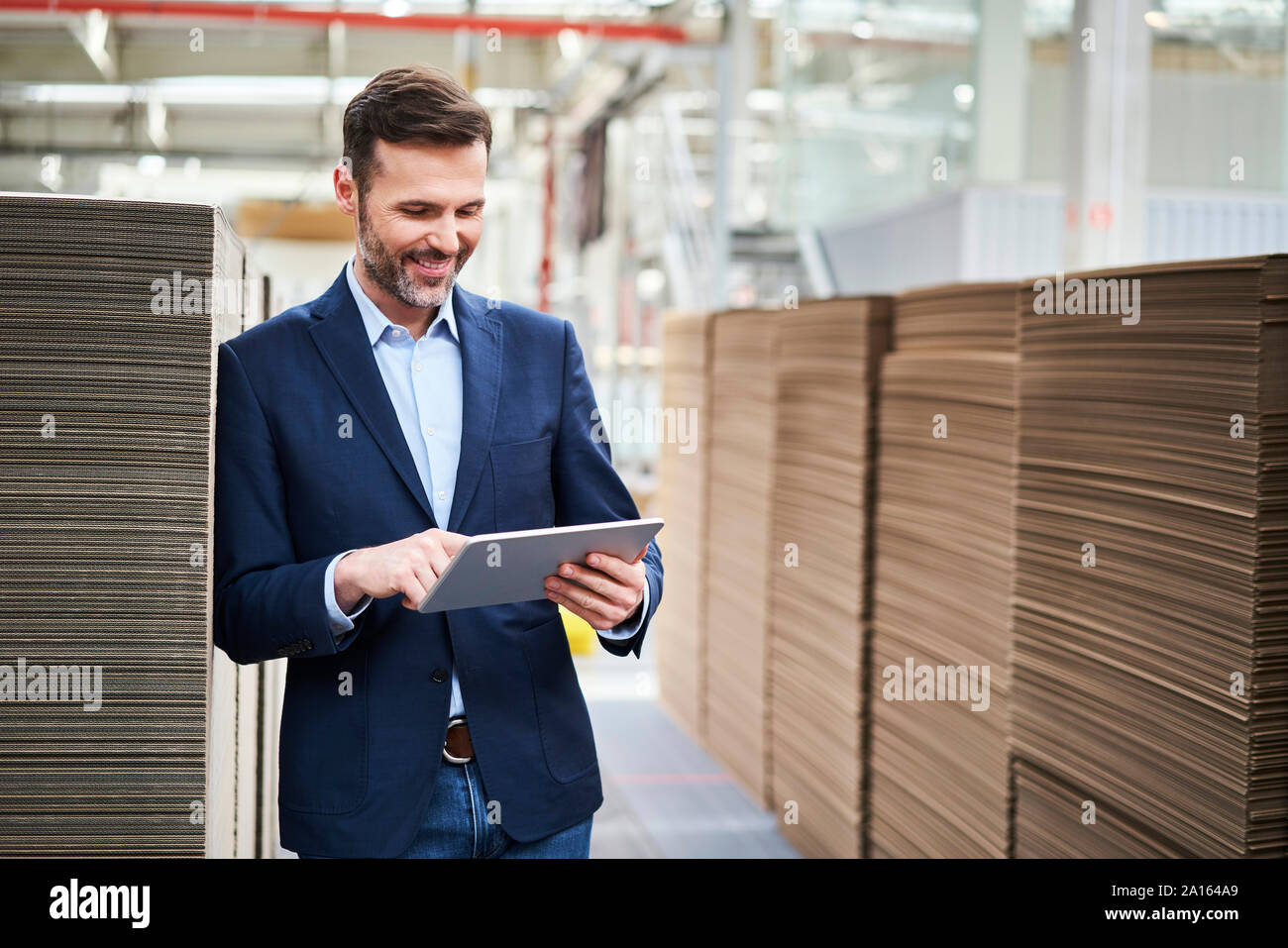 Imprenditore sorridente utilizzando tablet in magazzino di fabbrica Foto Stock