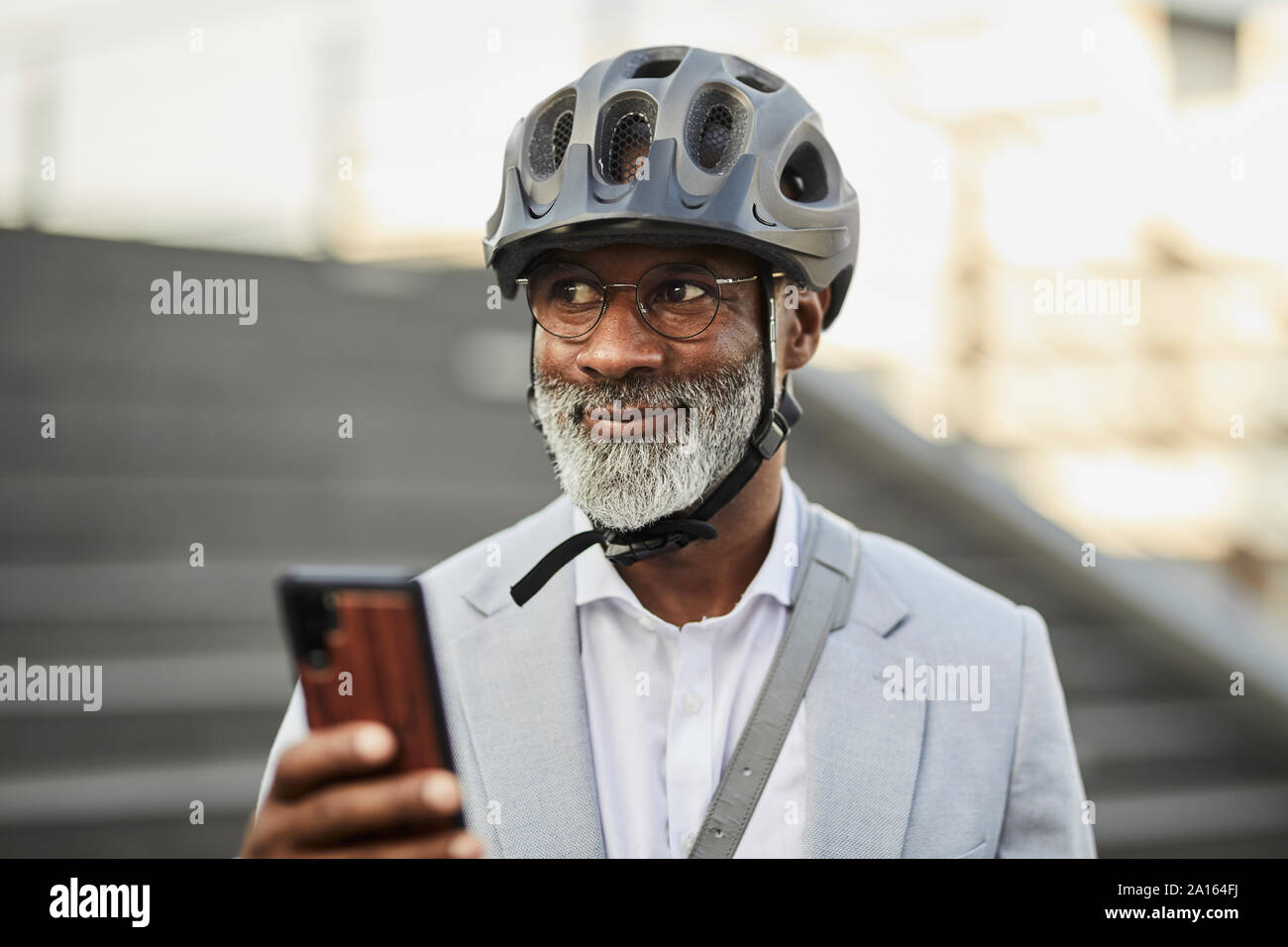 Ritratto di sorridente imprenditore maturo con lo smartphone che indossa il ciclismo casco e occhiali di protezione Foto Stock