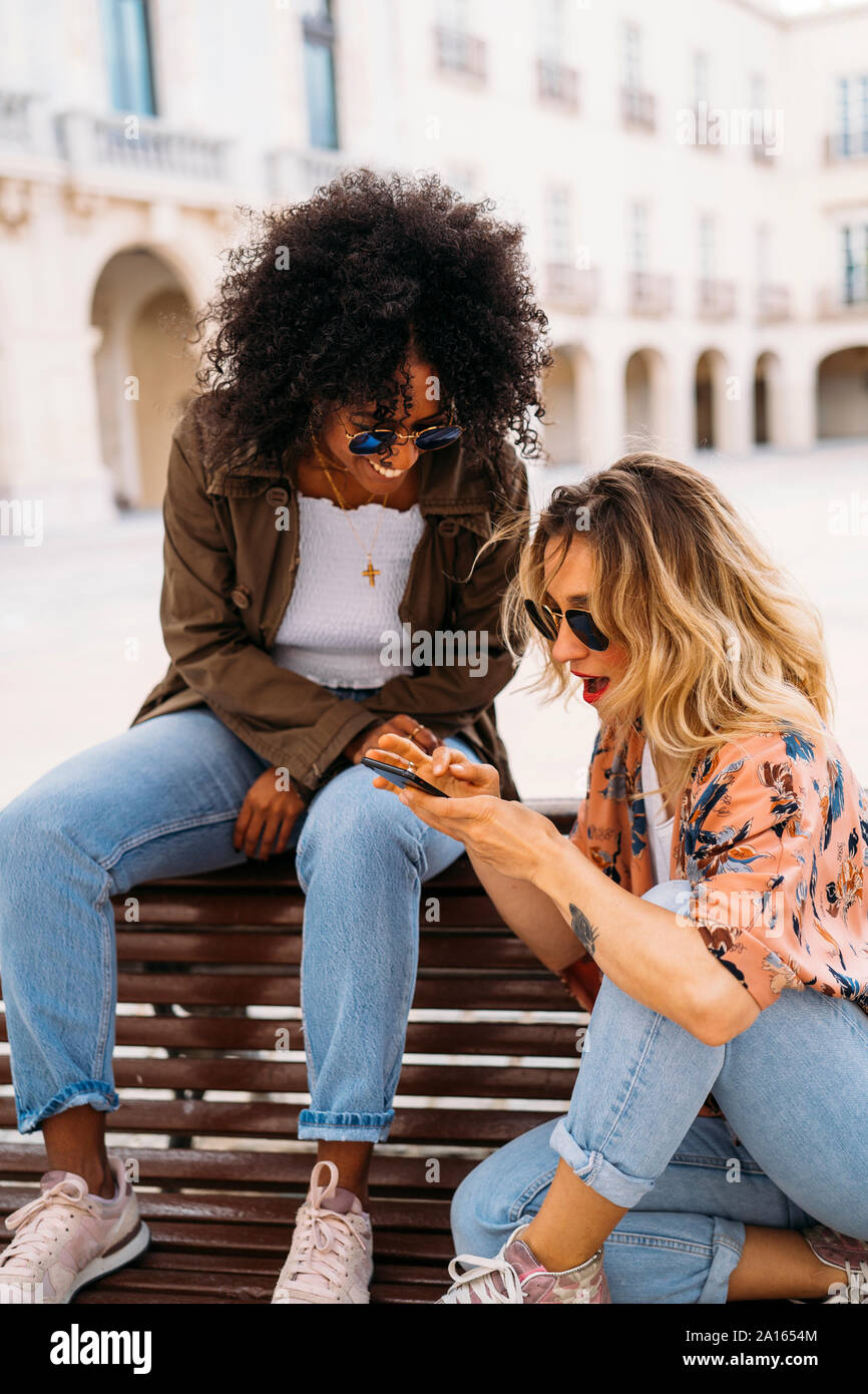 Multicultural felici donne parlare e utilizzare lo smartphone, seduta sul banco di lavoro Foto Stock