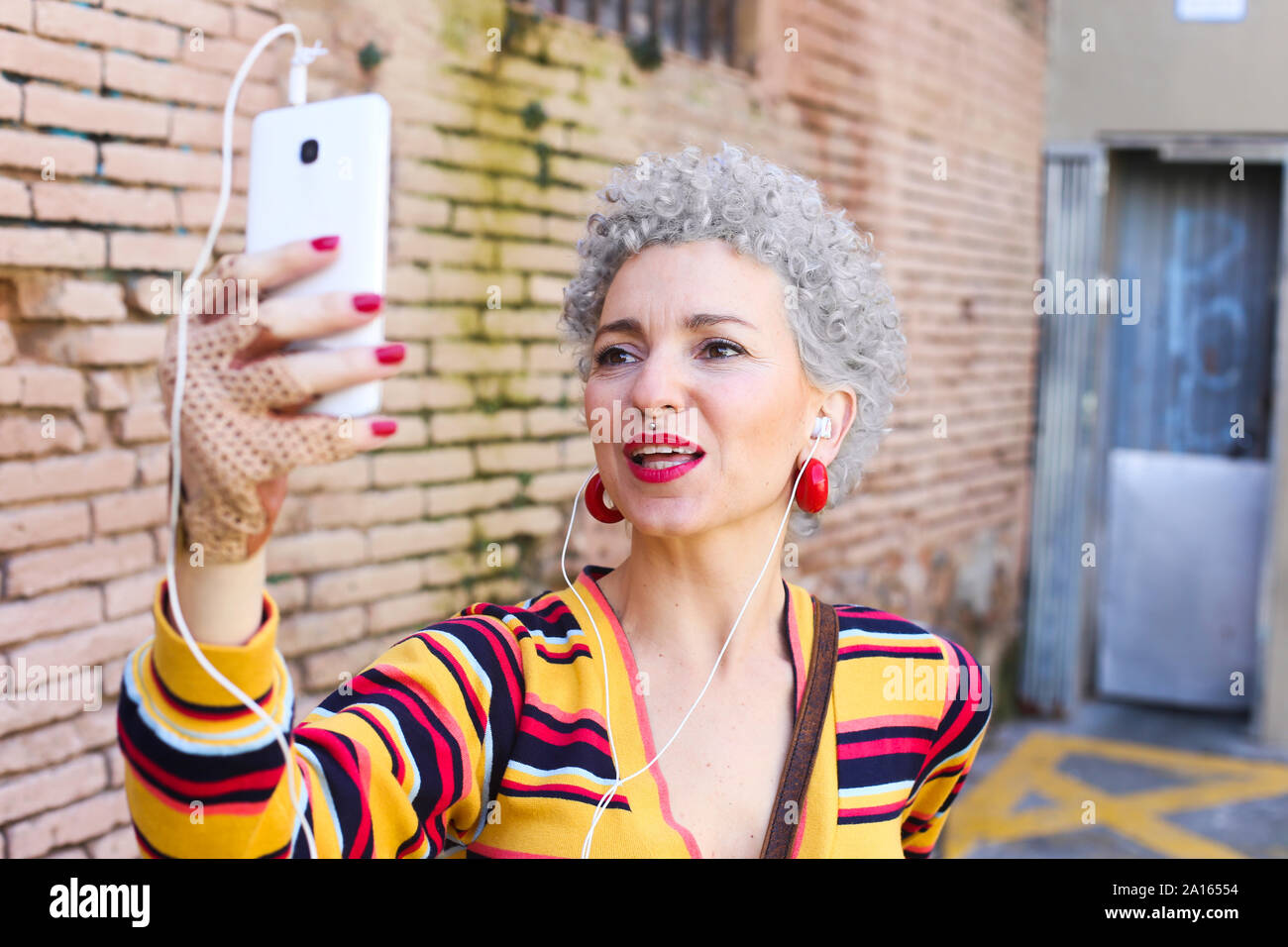 Ritratto di donna matura con labbra rosse e i capelli grigi tenendo selfie con un telefono cellulare Foto Stock