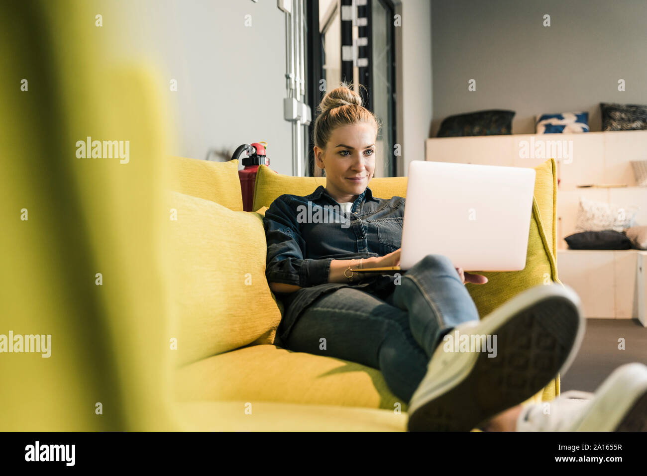 Casual imprenditrice utilizzando laptop sul lettino nella sala di office Foto Stock