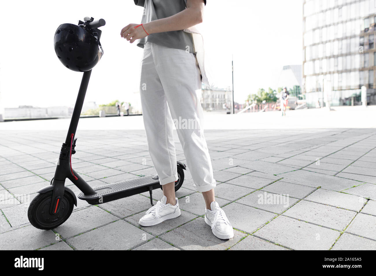 Giovane donna su e-scooter, edifici moderni in background Foto Stock