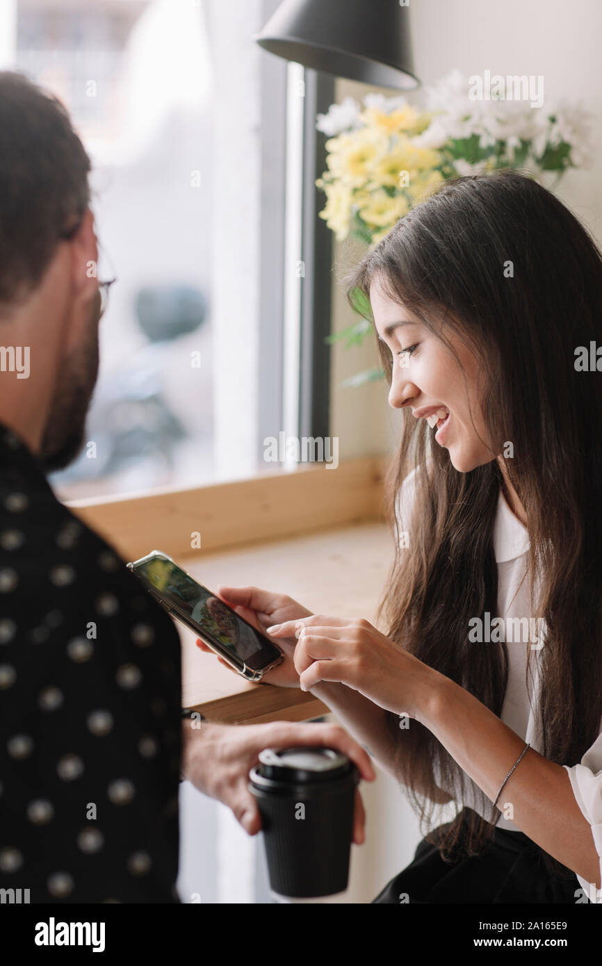 Coppia giovane con tazza monouso e smartphone in un cafe Foto Stock