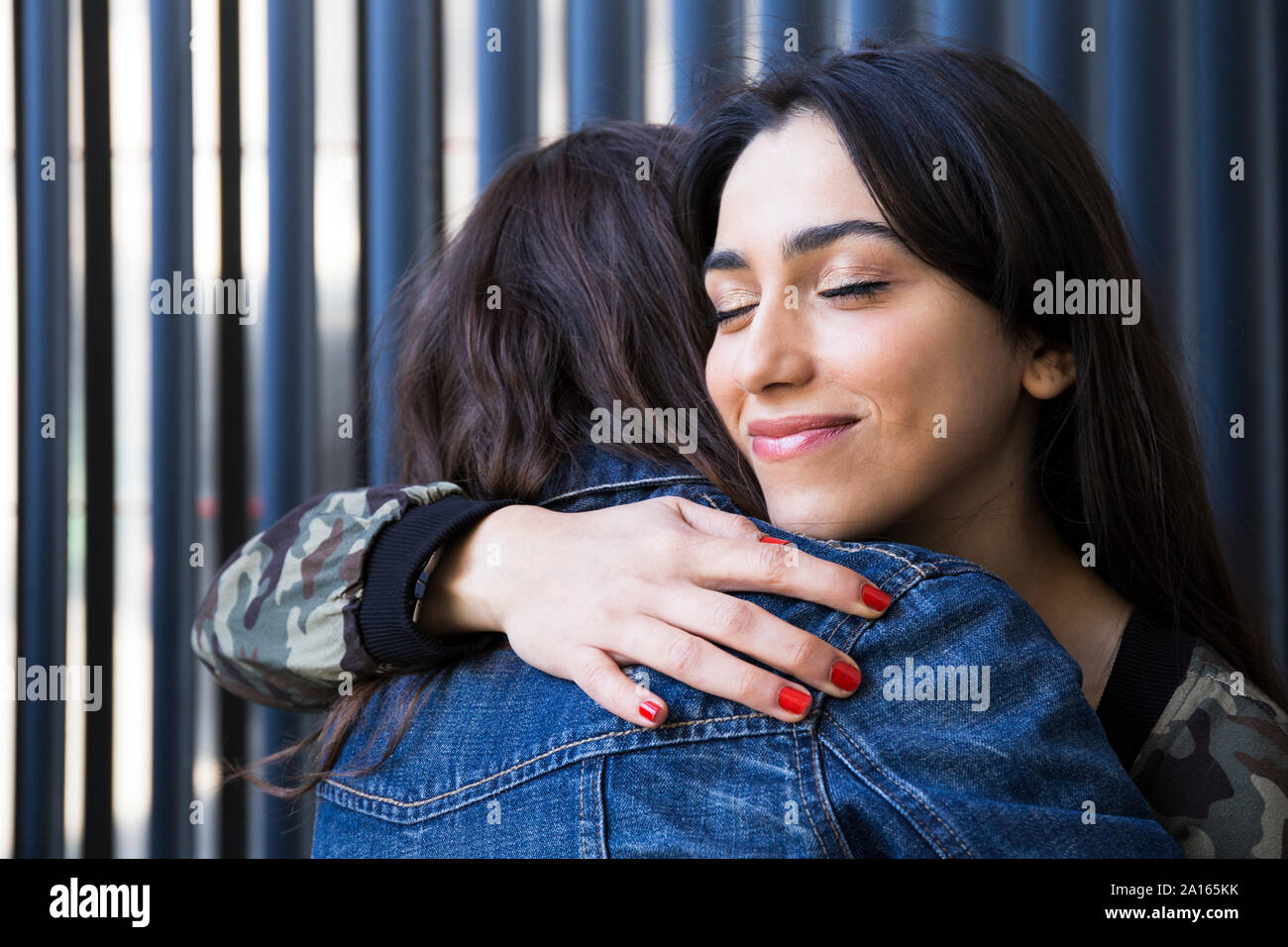 Giovani amici di sesso femminile con gli occhi chiusi abbracciando insieme in corrispondenza della parete Foto Stock