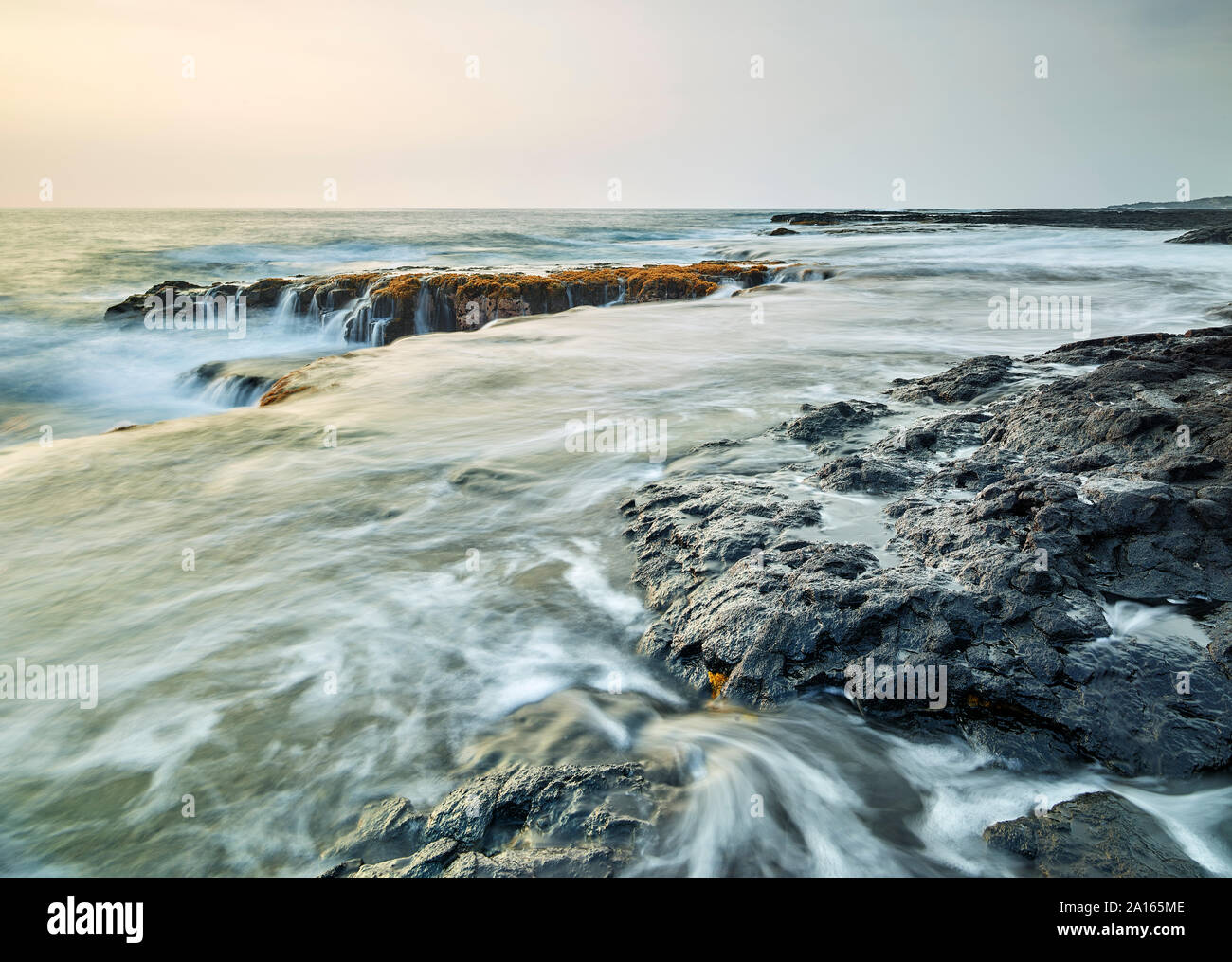 Spruzzi delle onde sulle rocce vulcaniche nella baia di Kealakekua contro sky durante il tramonto Foto Stock