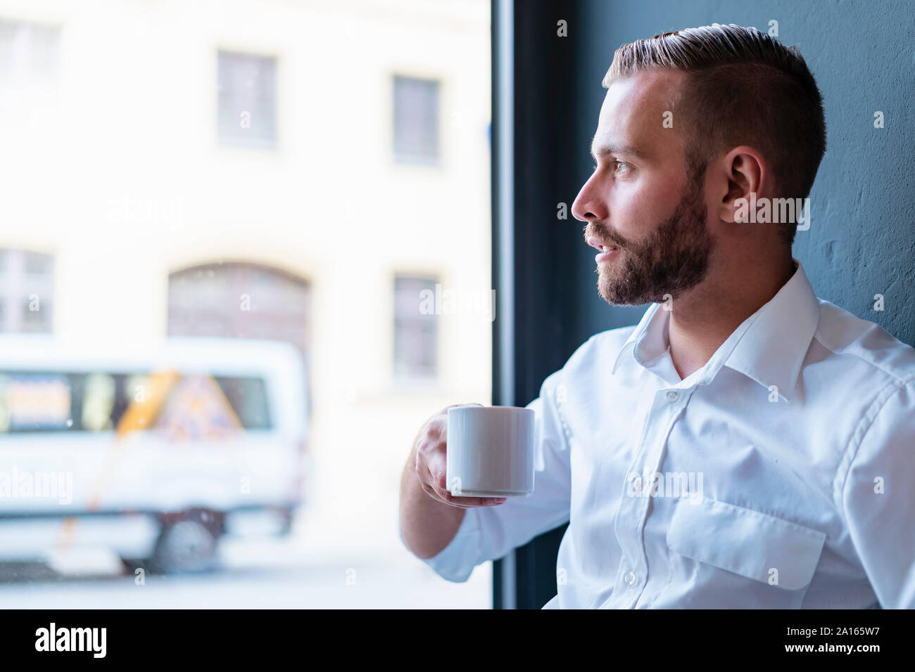 Imprenditore in ufficio avente una pausa caffè guardando fuori della finestra Foto Stock