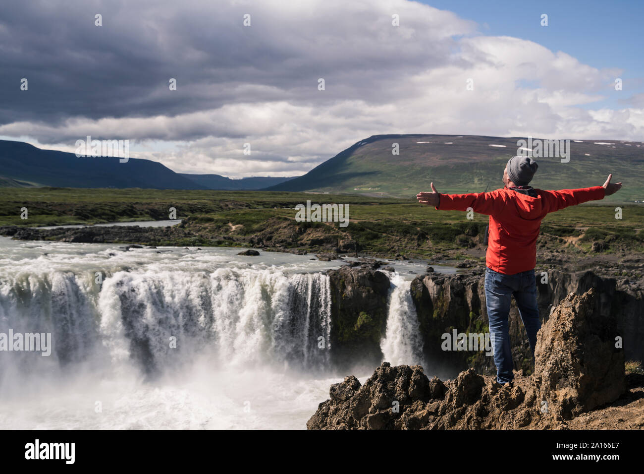 Uomo che guarda le cascate Godafoss, Islanda, con le braccia aperte Foto Stock