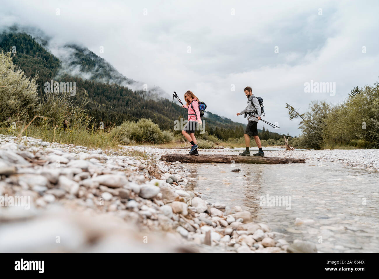 Una giovane coppia in un viaggio escursionistico Varcando il fiume su un registro, Vorderriss, Baviera, Germania Foto Stock