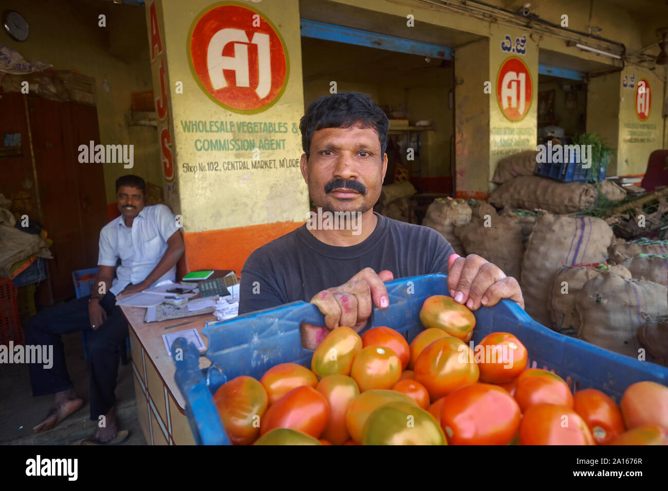 Un lavoratore di mercato con una cassa di pomodori, guardando un po' perplesso; presso il Mercato Centrale di Mangalore (Mangaluru), Karnataka, India Foto Stock