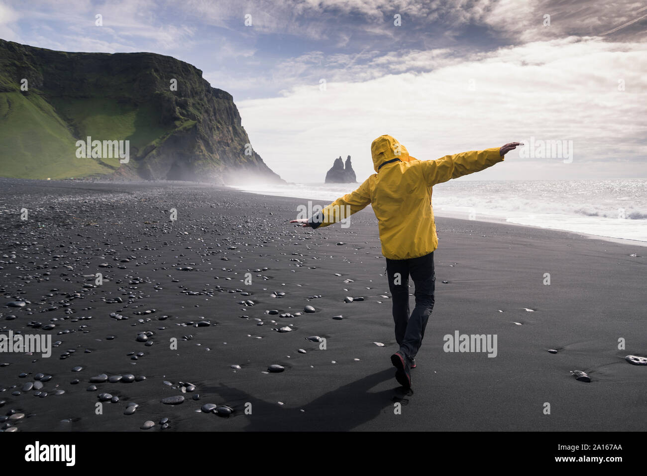 Uomo maturo a camminare su una spiaggia di lava in Islanda, con le braccia aperte Foto Stock