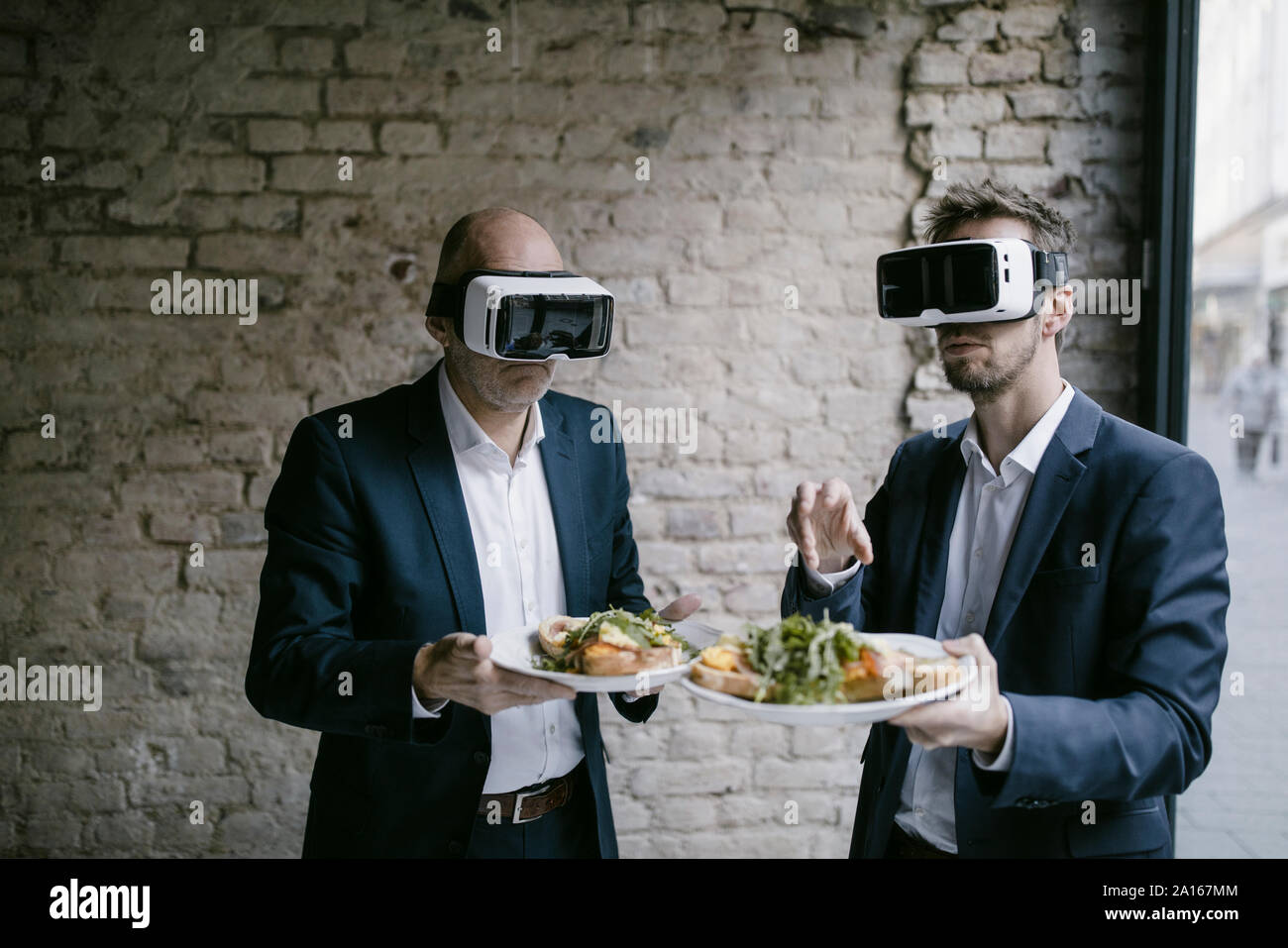 Senior e metà-imprenditore adulti indossando occhiali VR tenendo la piastra con un pasto Foto Stock