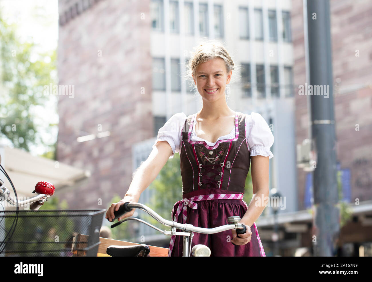 Ritratto di sorridere donna bionda con bicicletta indossando dirndl nella città di Friburgo, Germania Foto Stock