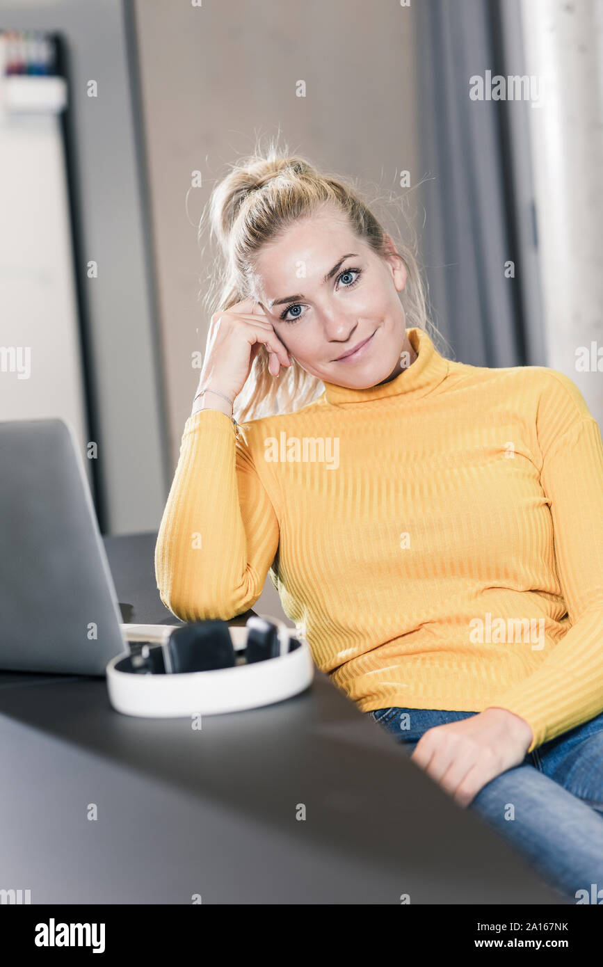 Ritratto di casual imprenditrice seduta a tavola in ufficio con computer portatile Foto Stock