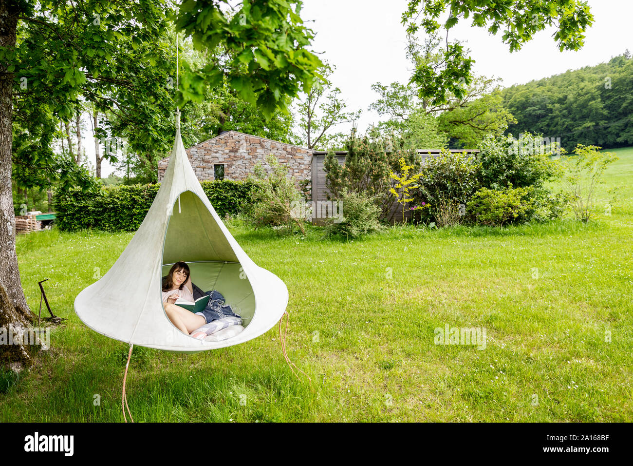 Rilassata donna libro di lettura in una tenda appesa Foto Stock