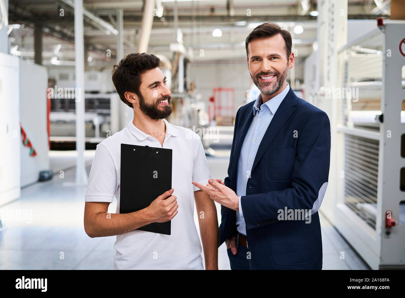 Ritratto di imprenditore sorridente e dipendente con gli appunti in una fabbrica Foto Stock