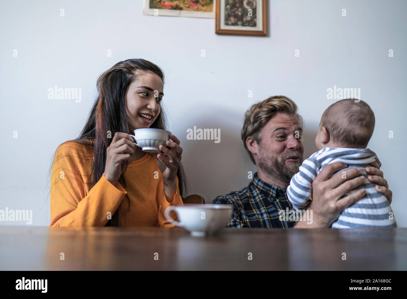 La famiglia felice con il bambino seduto al tavolo di legno a casa Foto Stock