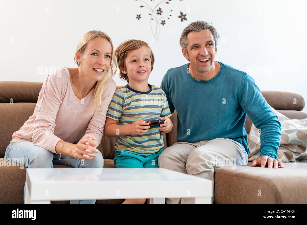 Genitori felici con il figlio la riproduzione di video gioco sul lettino a casa Foto Stock