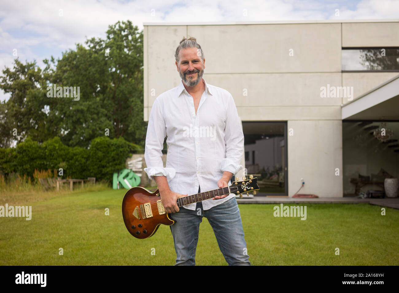 Ritratto di uomo maturo in piedi sul prato davanti a casa sua chitarra di contenimento Foto Stock