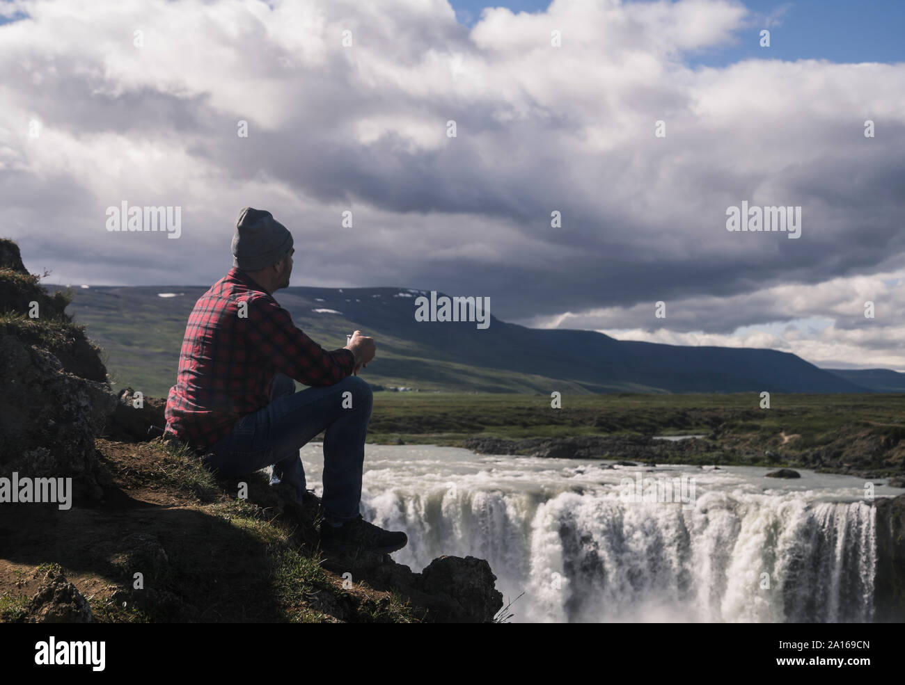Mann seduta con una tazza di caffè, guardando le cascate Godafoss, Islanda Foto Stock