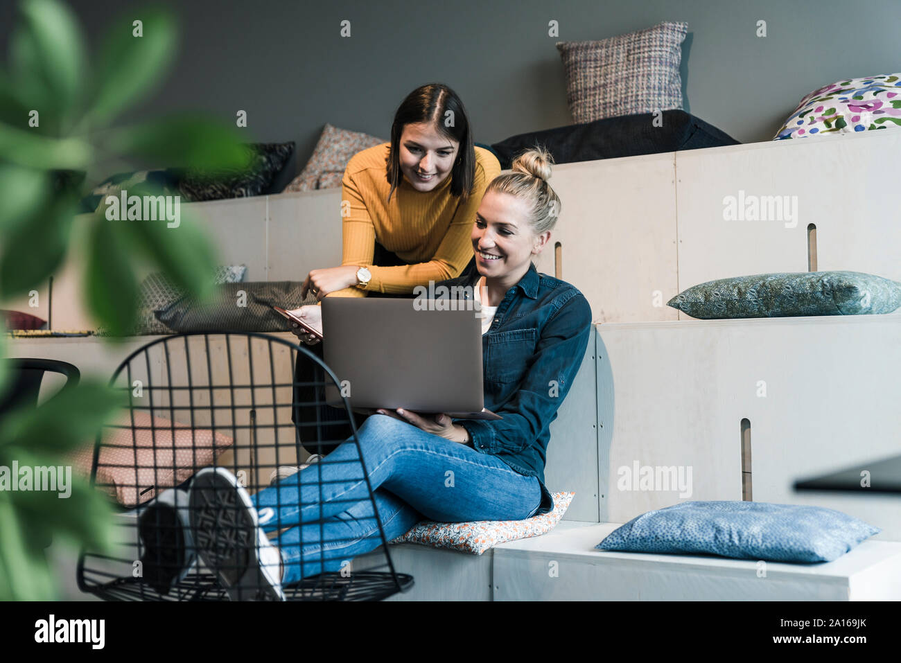 Due sorridente casual imprenditrici utilizzando computer portatile in ufficio lounge Foto Stock