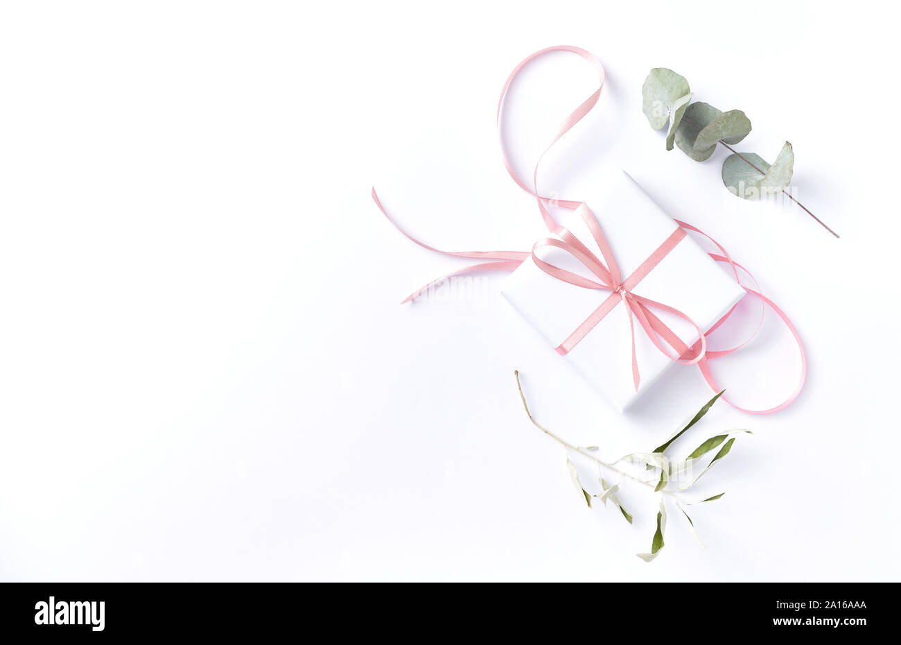 Scatola regalo bianca con nastro rosa e asciugare le foglie di eucalipto su sfondo bianco. Lay piatto. Spazio di copia Foto Stock