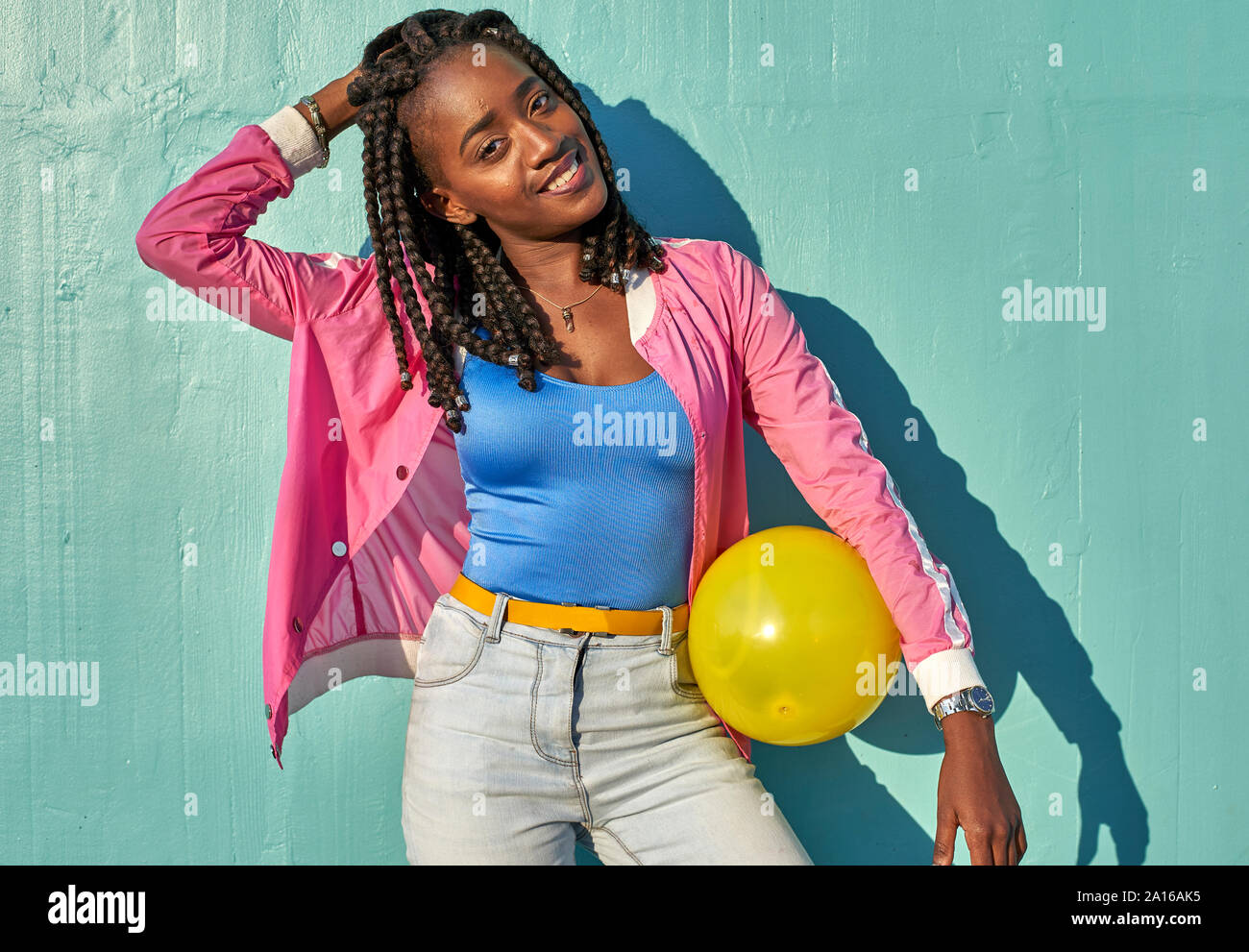 Giovane donna nera con una sfera gialla davanti a una parete blu Foto Stock