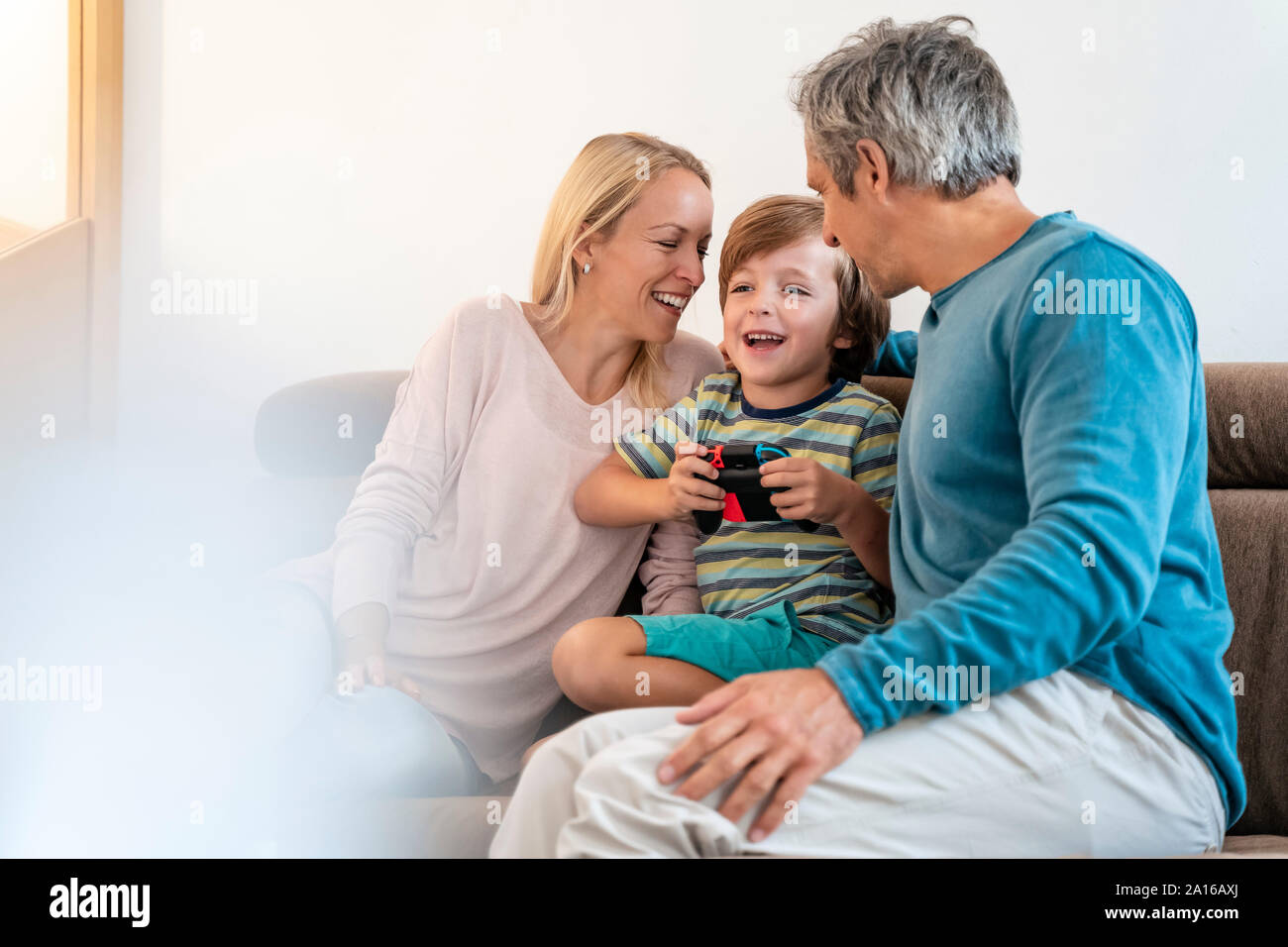 Genitori felici con il figlio la riproduzione di video gioco sul lettino a casa Foto Stock