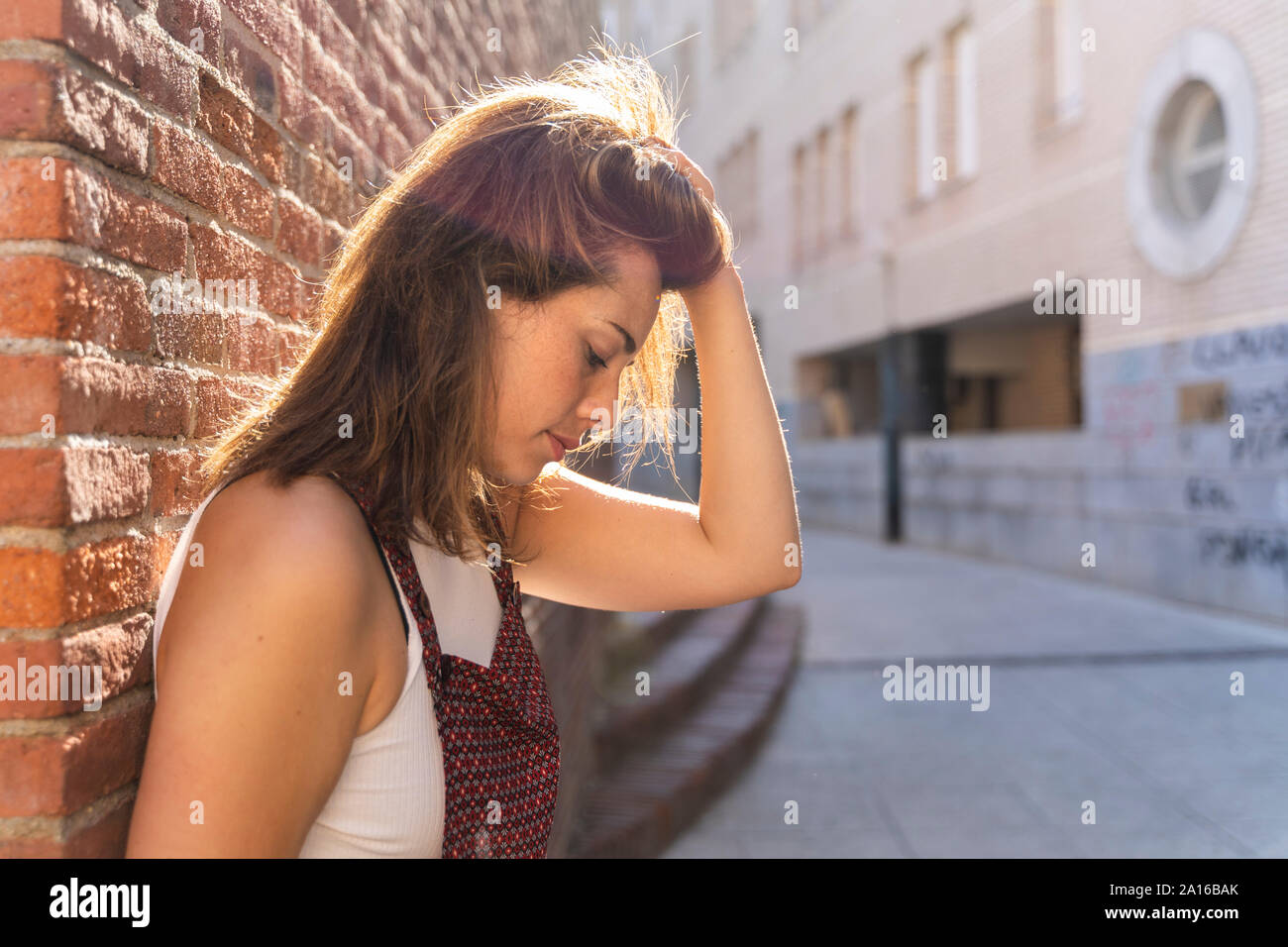 Giovane donna appoggiato su di un muro di mattoni, mano nei capelli Foto Stock