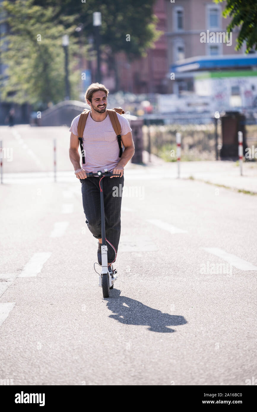 Giovane uomo che cavalca scooter elettrico sulla strada Foto Stock