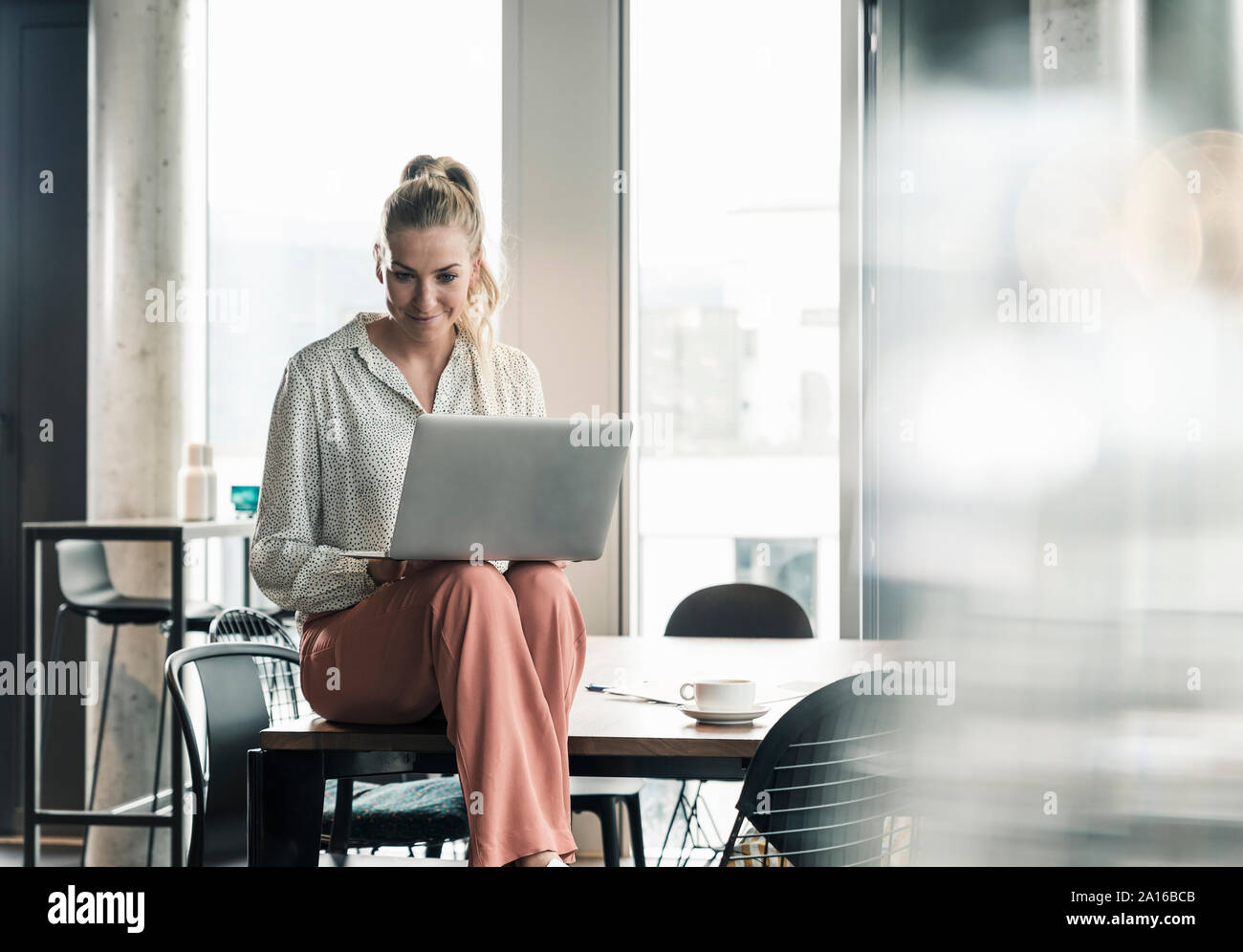 Imprenditrice seduta sul tavolo in ufficio utilizzando laptop Foto Stock