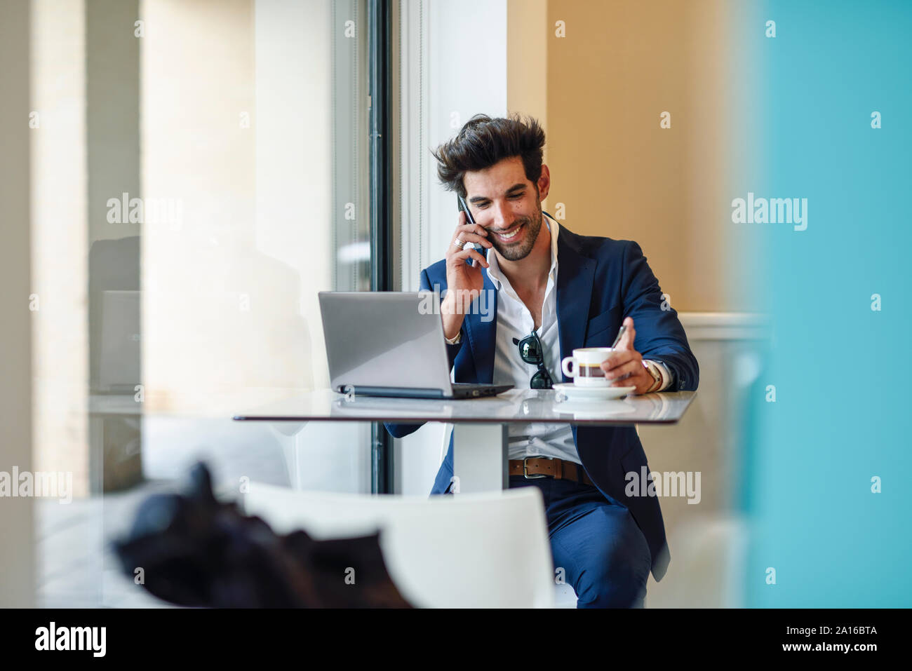 Imprenditore sorridente con notebook e smartphone in un urbano cafe Foto Stock