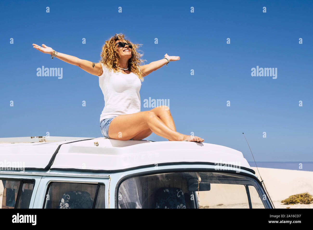 Donna seduta sul tetto di un furgone, a braccia alzate Foto Stock