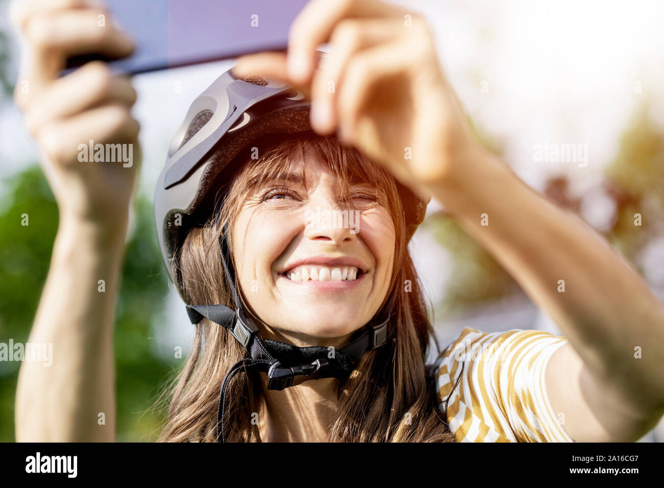 Donna felice di indossare il casco per bicicletta prendendo un selfie Foto Stock Donna felice di indossare il casco per bicicletta prendendo un selfie Foto Stock