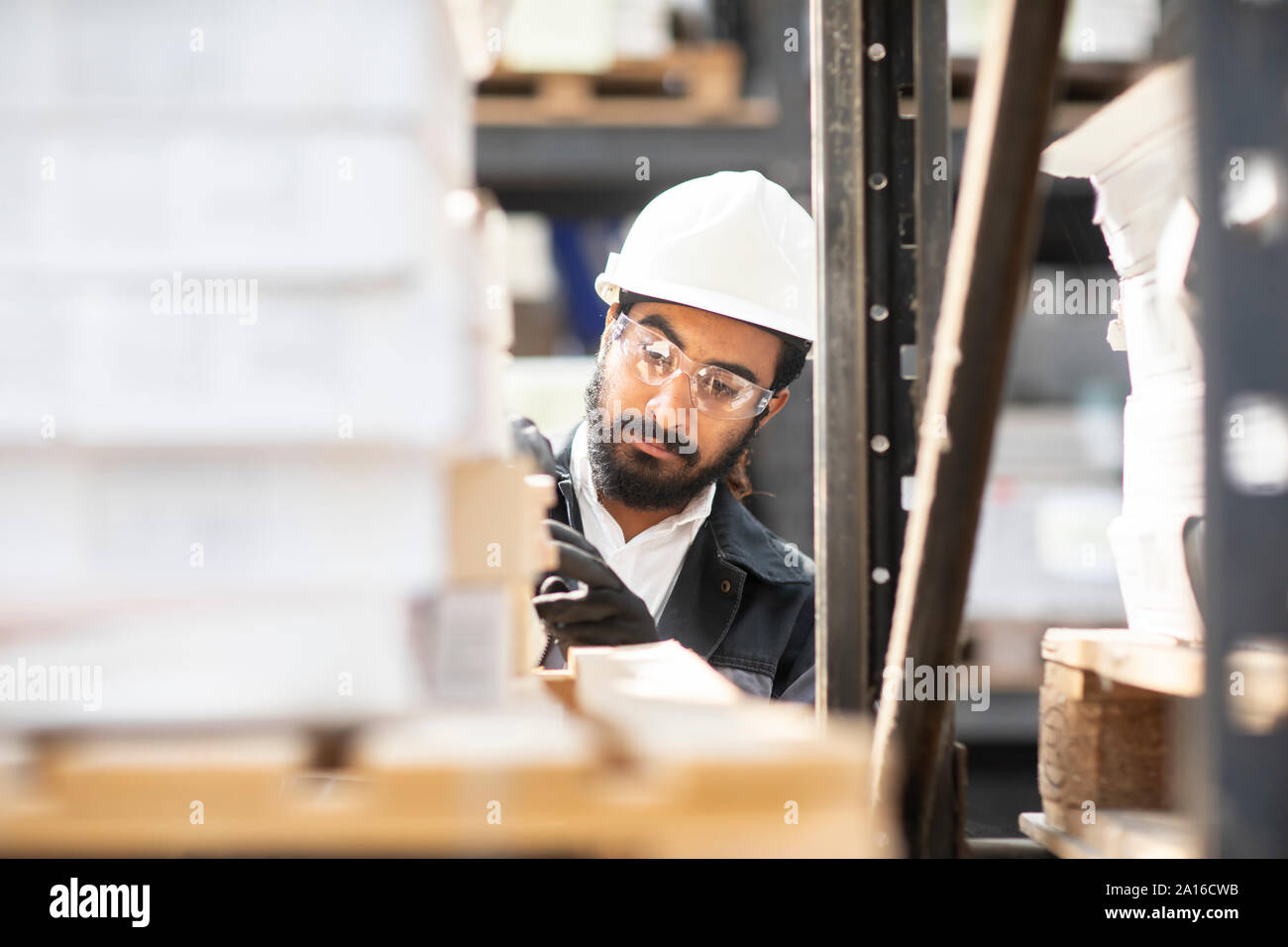 Giovane uomo indossare elmetto lavorando in un magazzino Foto Stock