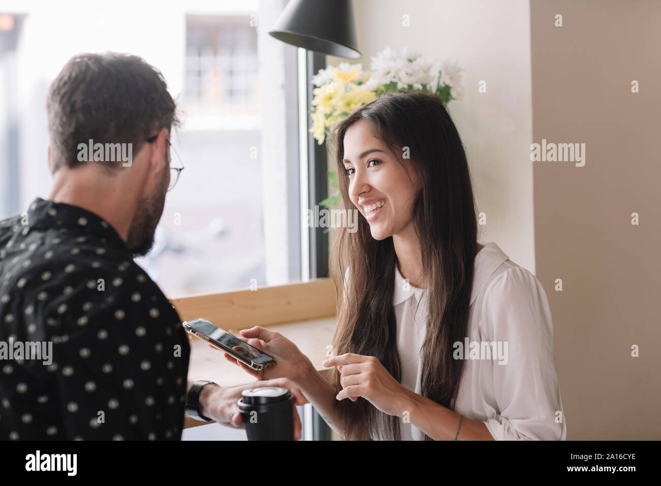 Coppia giovane con tazza monouso e smartphone in un cafe Foto Stock