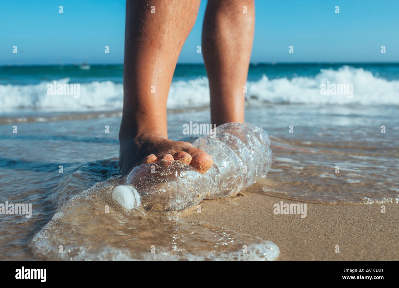 Piedi di uomo intensificazione su Svuotare la bottiglia di plastica che giace sulla spiaggia, close-up Foto Stock