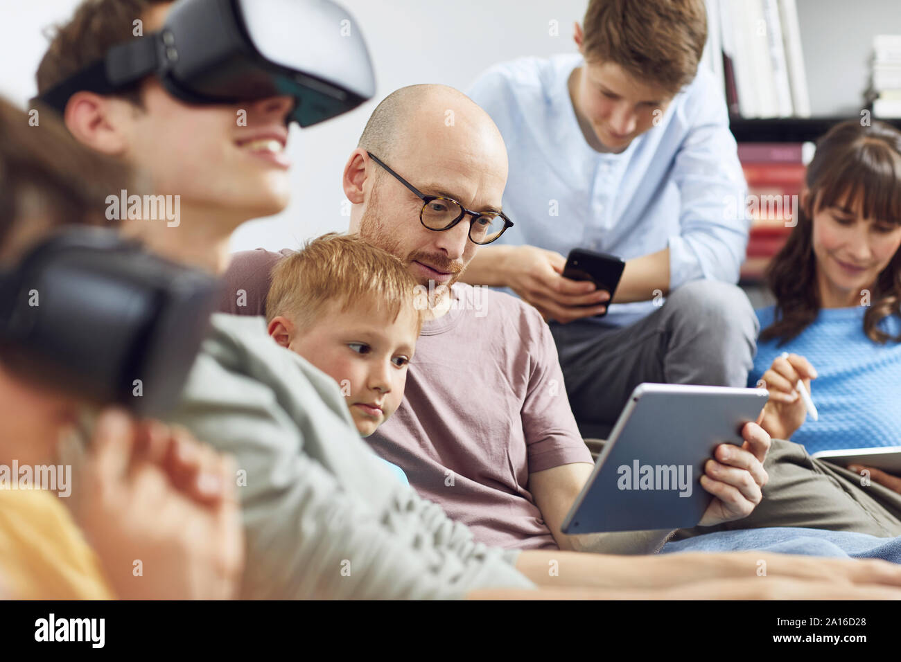 La famiglia felice seduta sul lettino, utilizzando gli occhiali VR e dispositivi mobili Foto Stock