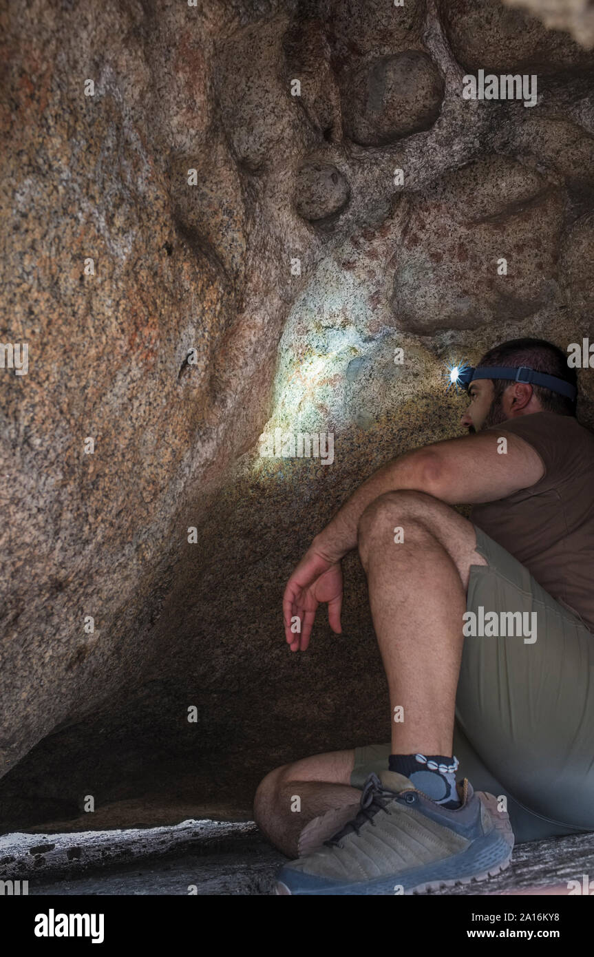 L'uomo osservando lo schema di epoca preistorica all'interno dipinti del masso di granito a monumento naturale di los Barruecos, Estremadura, Spagna Foto Stock