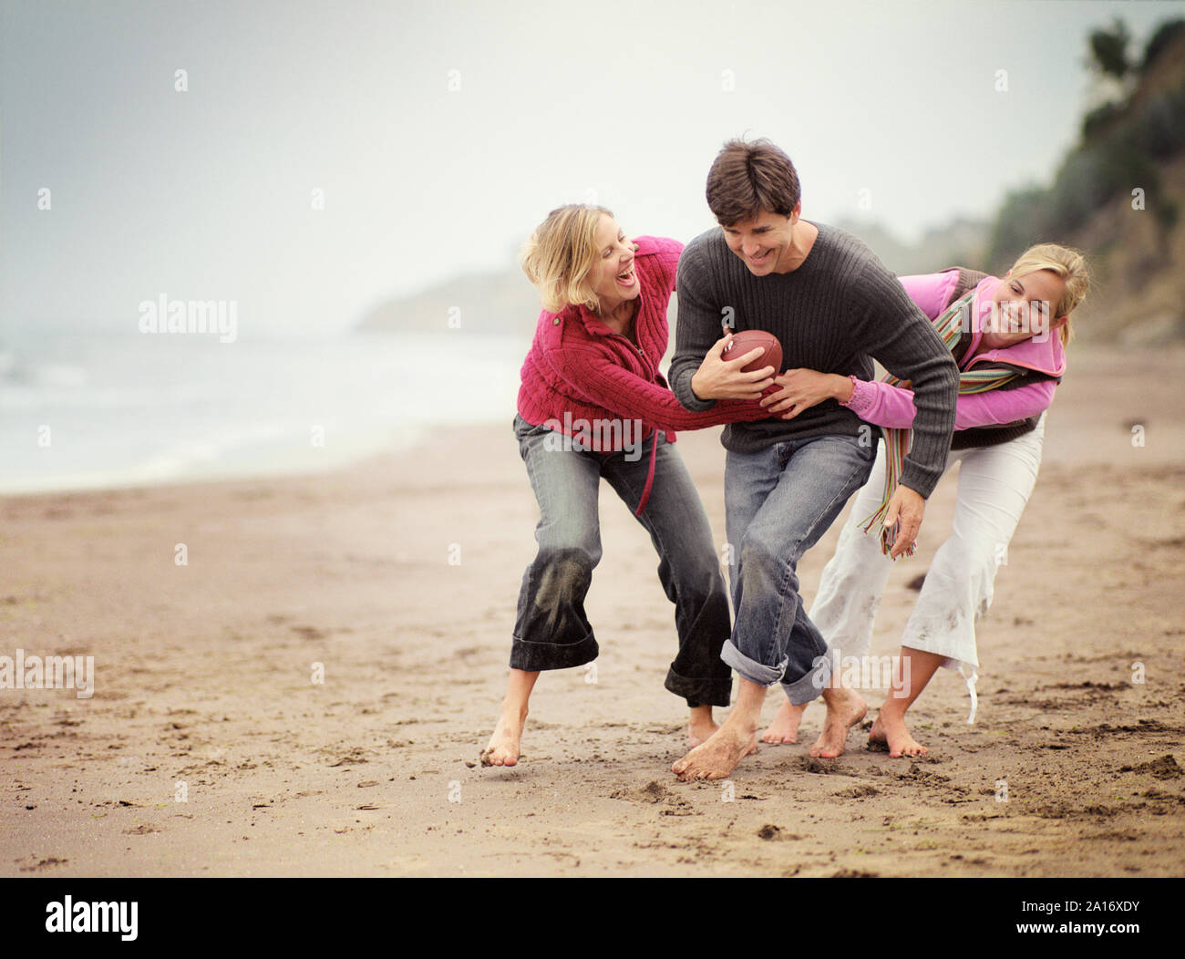 Mid-adulto giovane con la loro figlia adolescente a giocare una palla di gioco lungo una spiaggia. Foto Stock