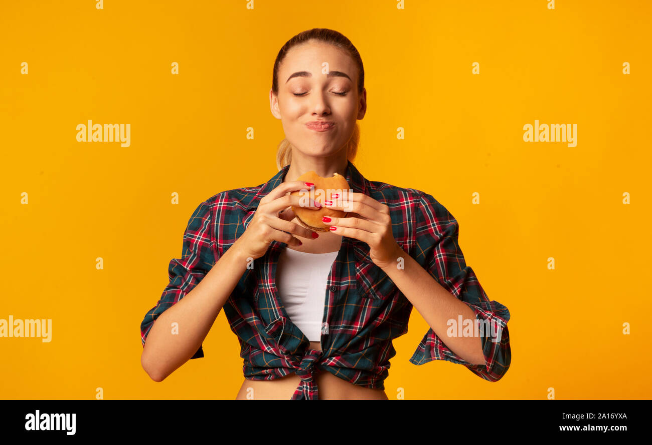 Giovane donna di mangiare hamburger in piedi in Studio Foto Stock