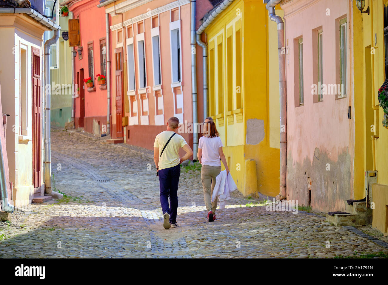 Due persone che camminano il colorato conserve di facciate di case con strada acciottolata in salita in cittadella di Sighisoara, Romania. Sighisoara, Romania - Foto Stock