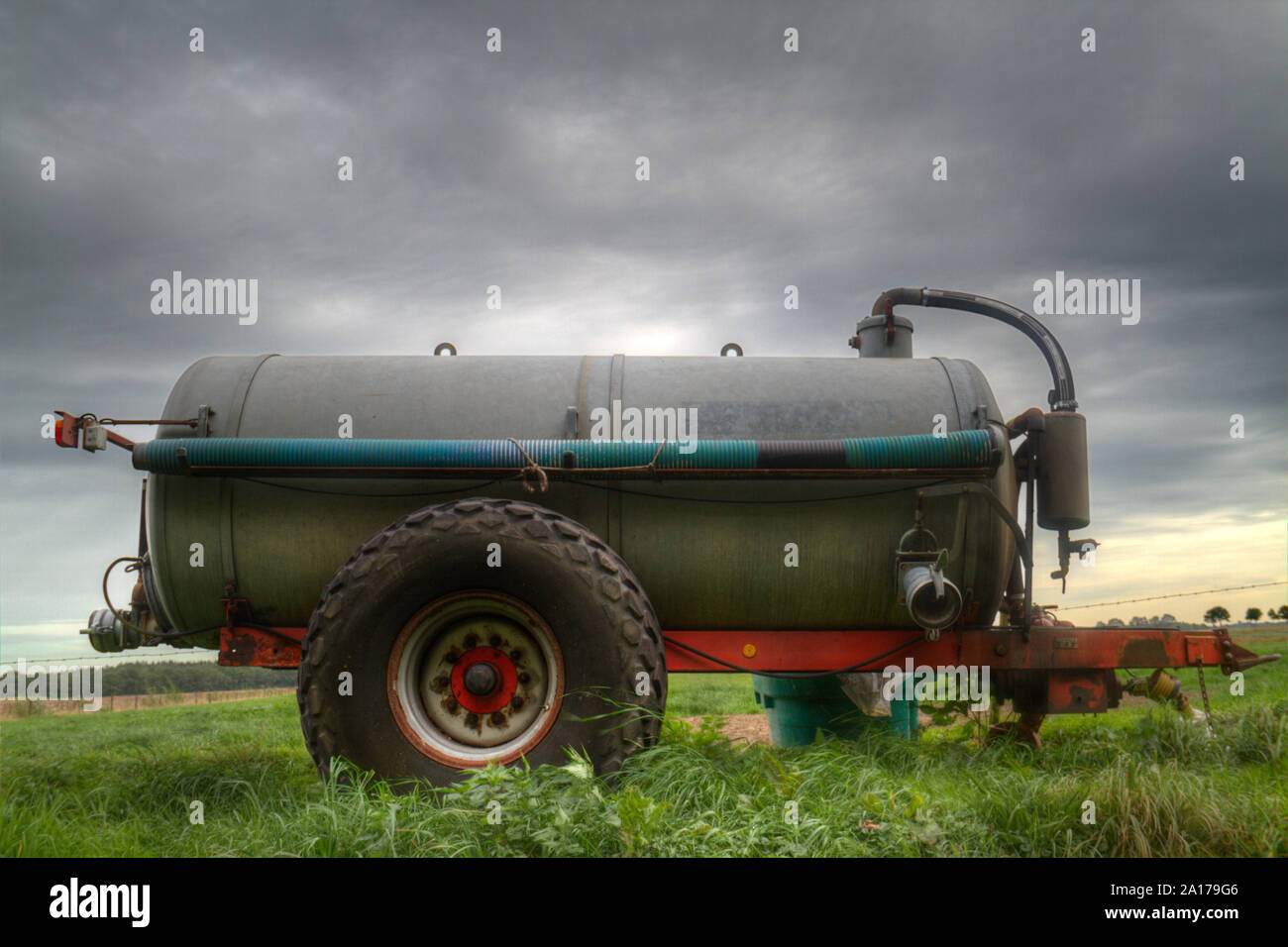 Grigio e rosso autocisterna spandiliquame in un campo sotto un cielo minaccioso Foto Stock