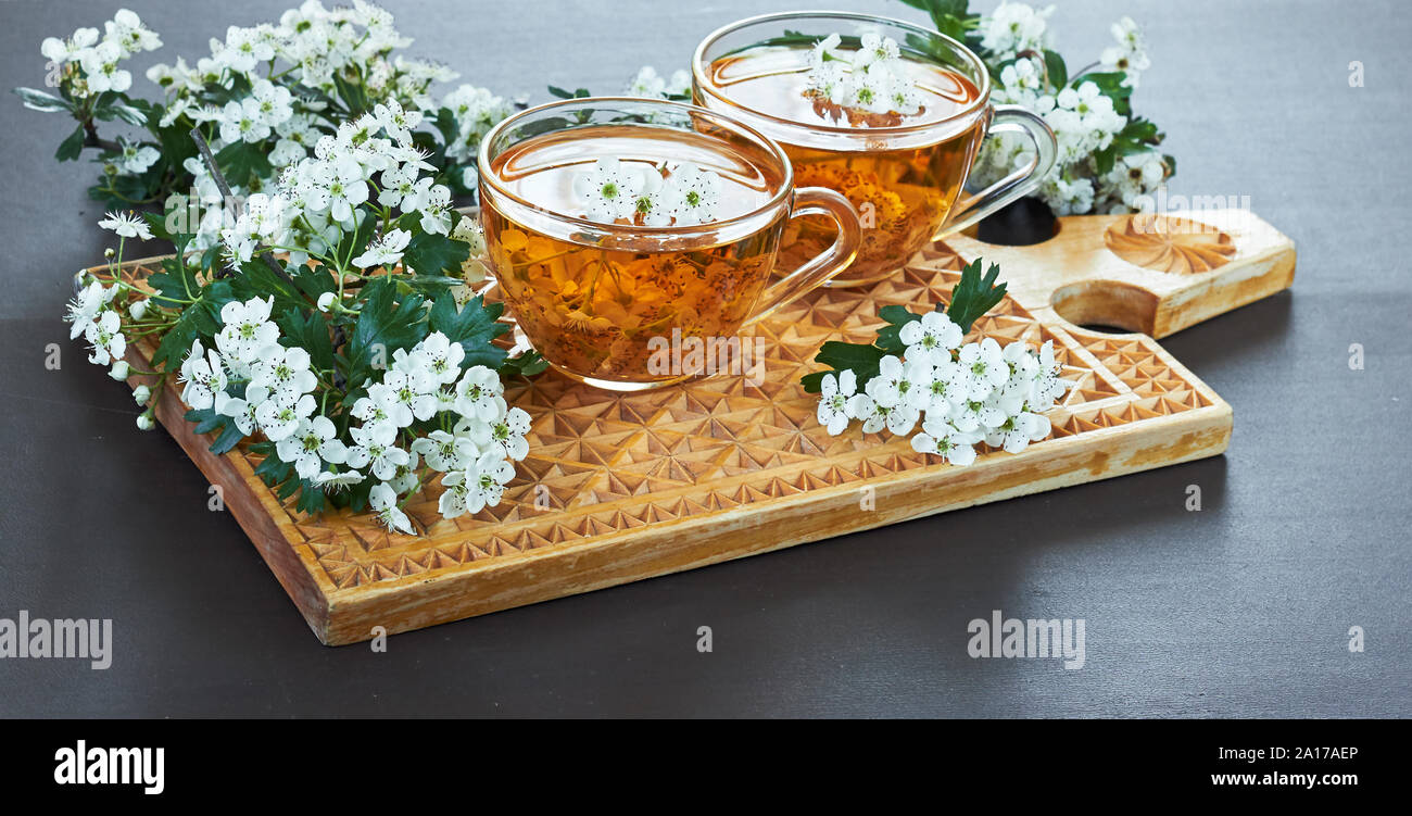 Due tazze di fiore di erbe da tè haw thorn blossom sul tagliere di legno su sfondo nero, cardiovascolare dring guarigione medicina alternativa c Foto Stock