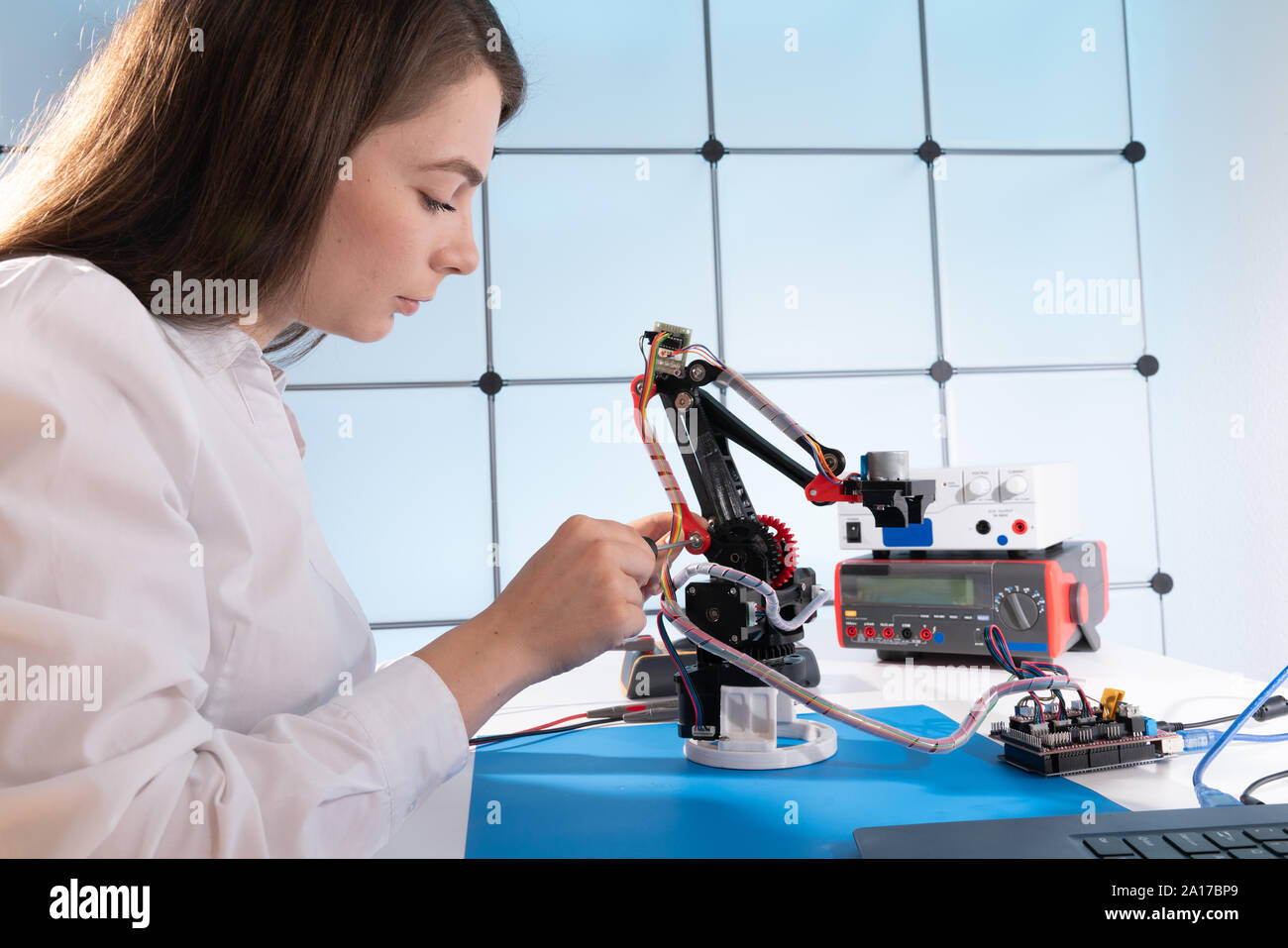 Una giovane donna scrive un algoritmo per il braccio del robot. La scienza laboratorio di ricerca per il braccio robotico modello. Laboratorio di Computer Foto Stock
