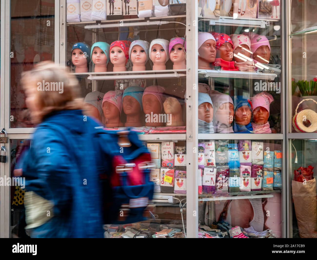 Mosca, Russia - 14 Settembre 2019: una donna cammina davanti a un piccolo negozio di strada. Vetrina con le teste dei manichini. Vendita di cappelli, calze e calzini Foto Stock