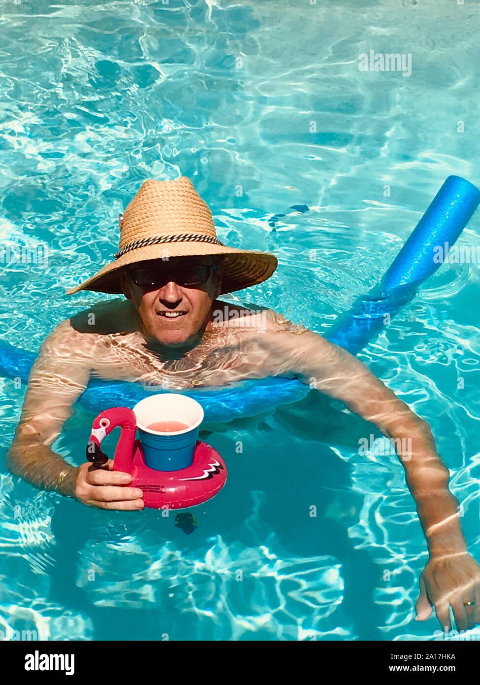L'uomo godendo il tempo in piscina indossando un cappello per il sole con un galleggiante portabicchiere contenente un punch alla frutta Bevande Foto Stock