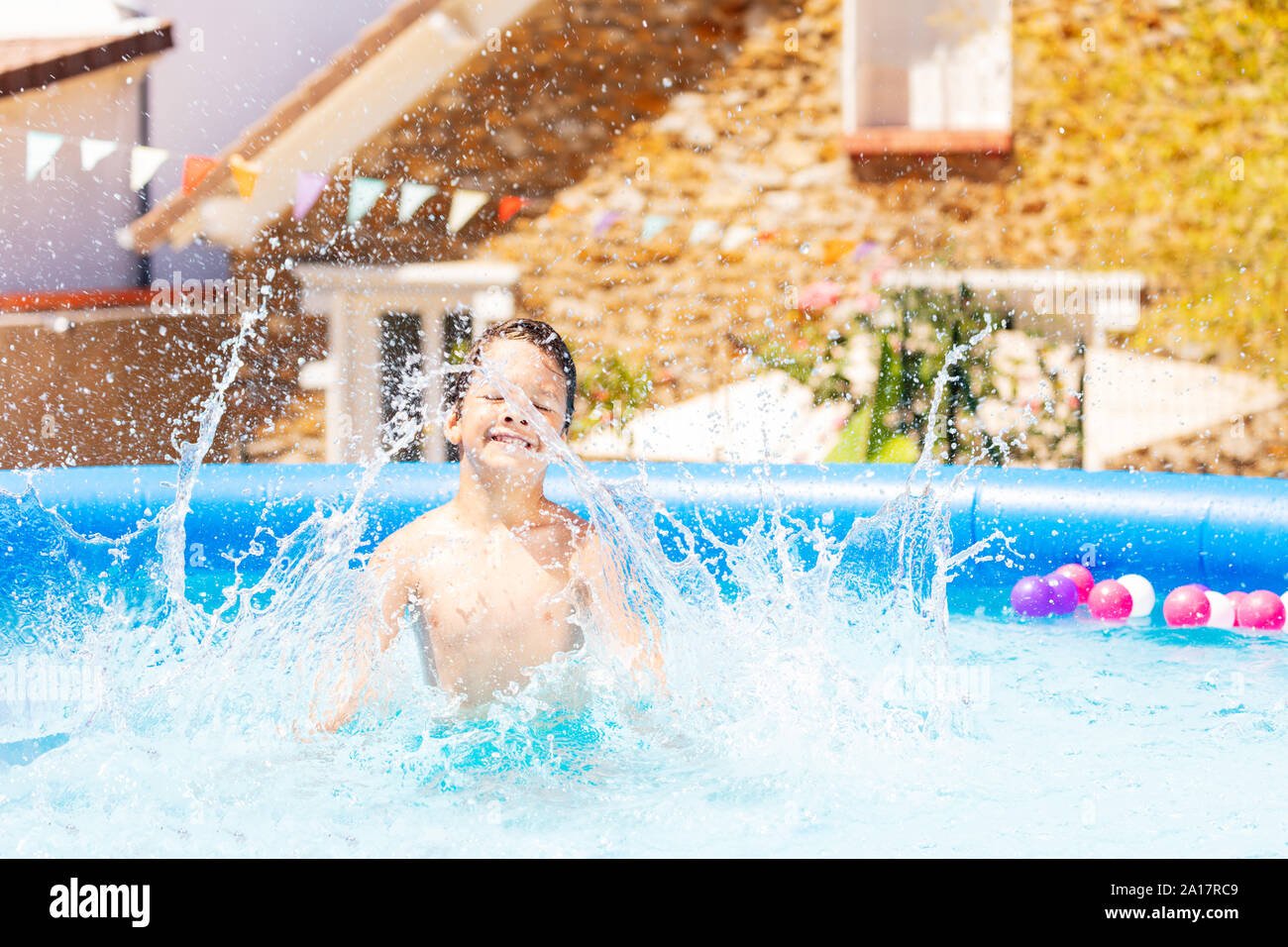 Ritratto di un ragazzo divertirsi in piscina facendo grandi schizzi con la sua casa sullo sfondo Foto Stock